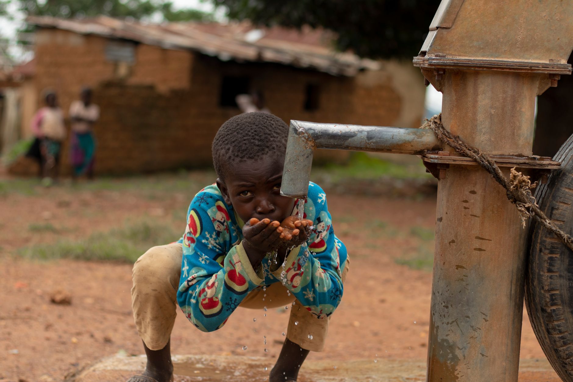 A boy drinks water from his cupped hands at a village handpump