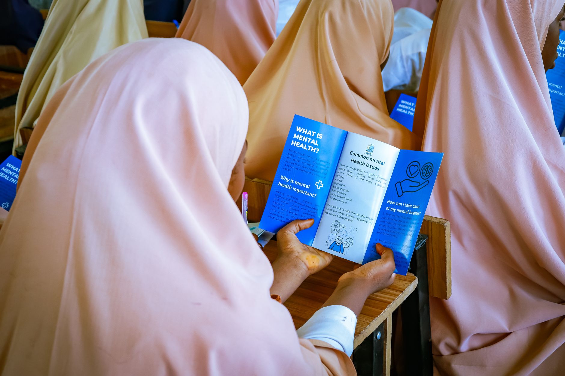 Schoolgirls in headscarves read a leaflet about mental health in a classroom