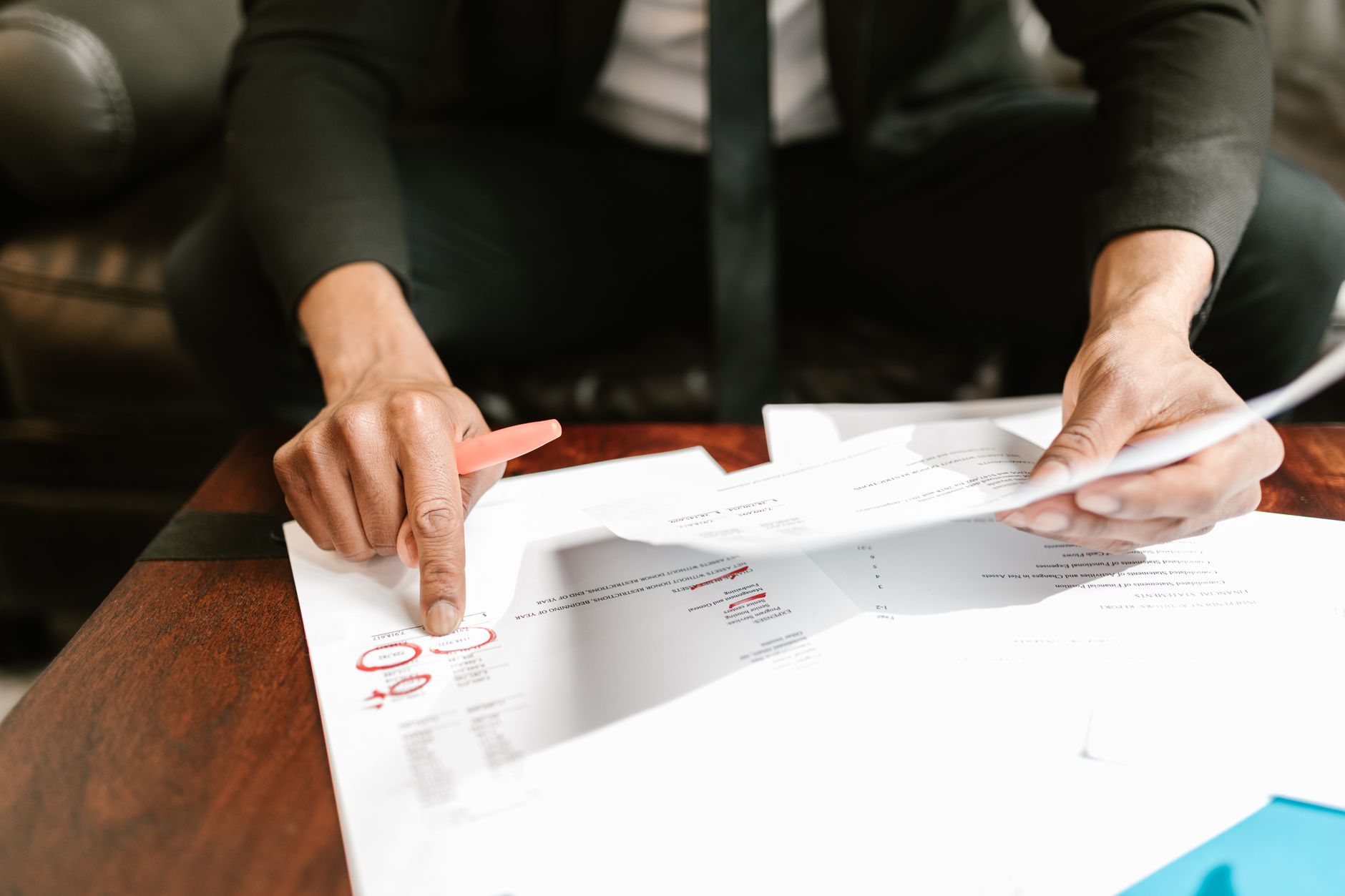 A person points with an orange pen at figures circled in red on a printed document
