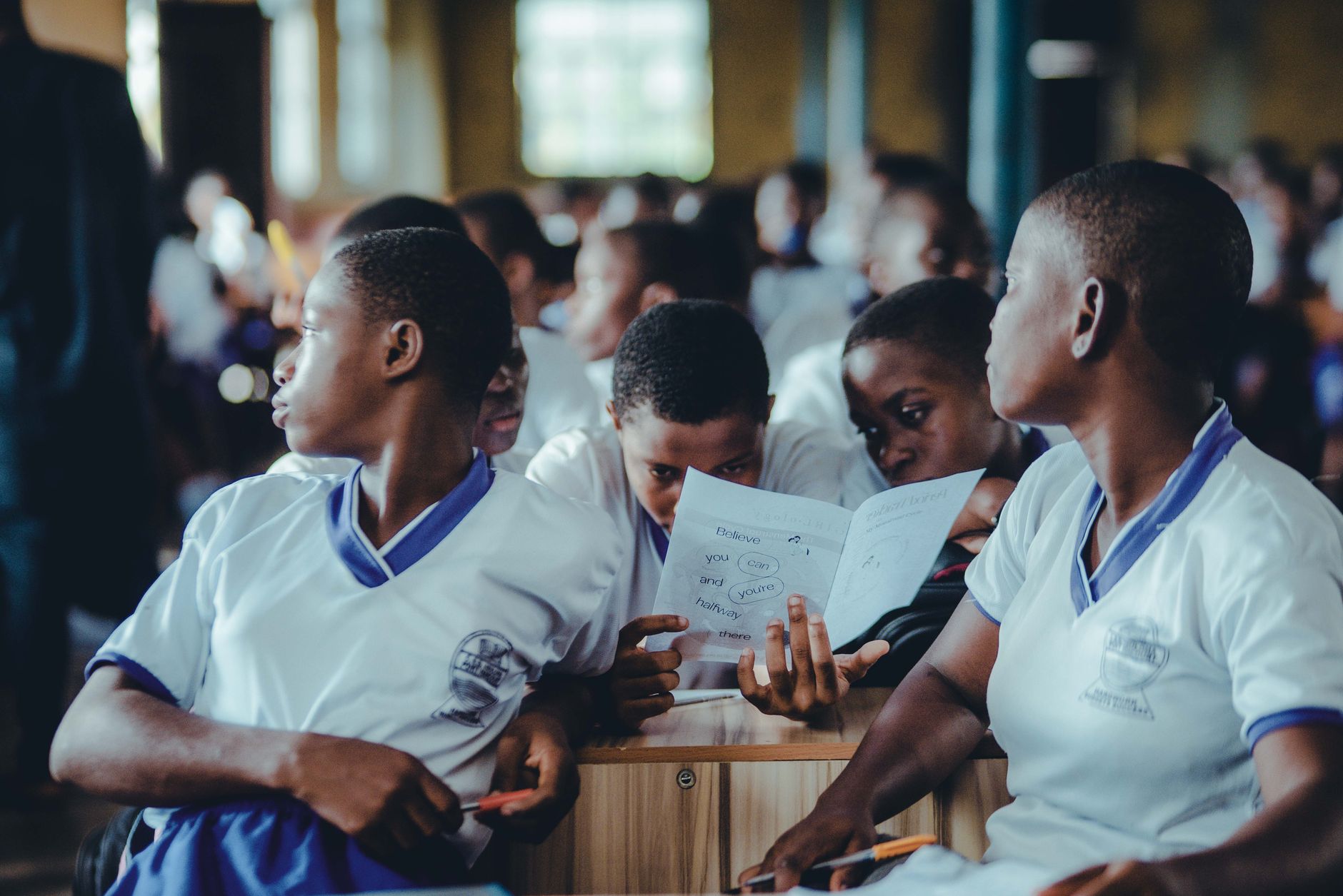 Schoolgirls in white and blue uniforms read a handout together in a classroom