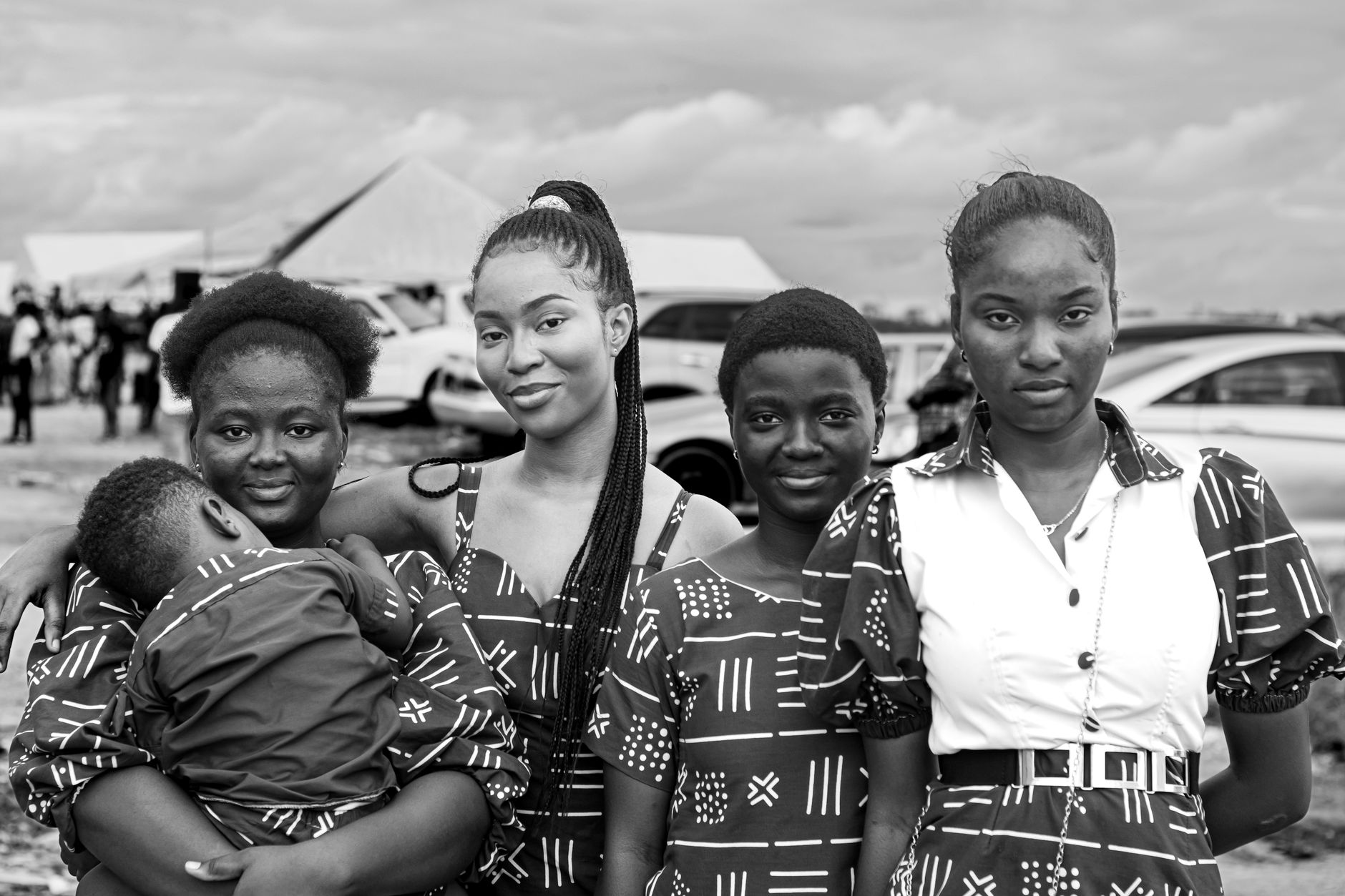 Black-and-white portrait of four young women in matching patterned dresses, one holding a small child