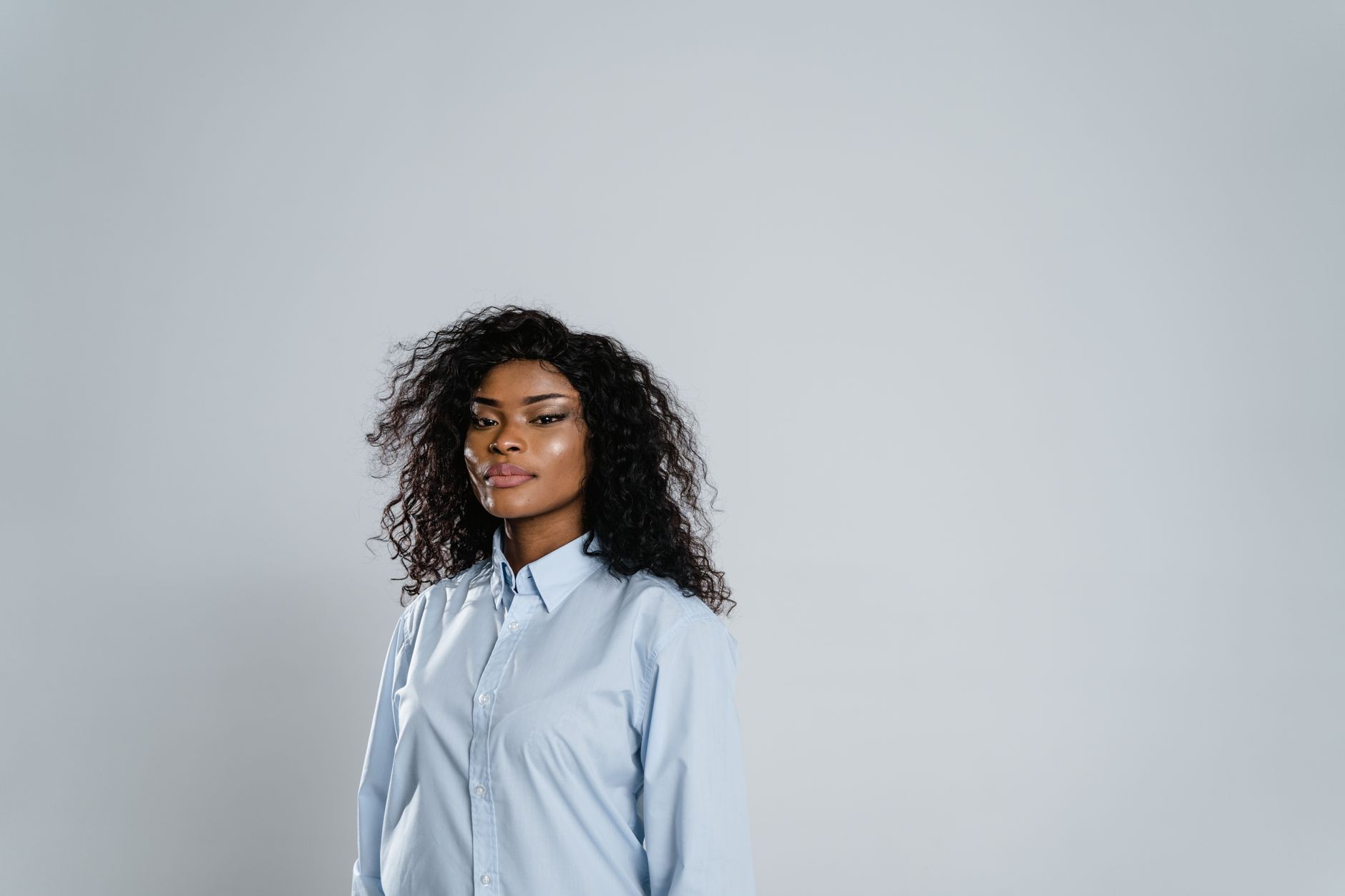 Portrait of a woman with curly hair in a light blue shirt against a grey background