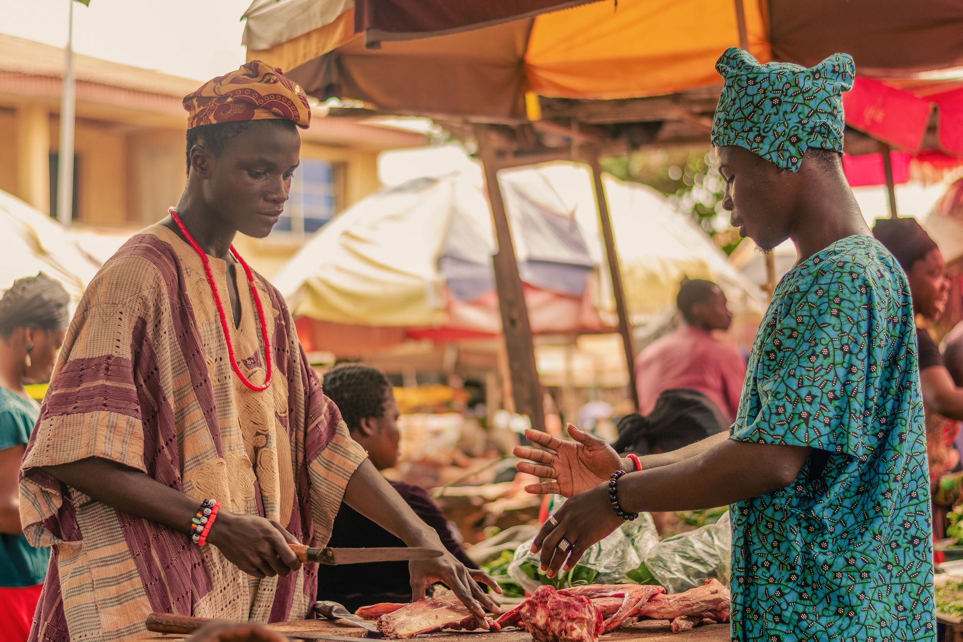 A trader cuts meat at an open-air market stall as a customer looks on