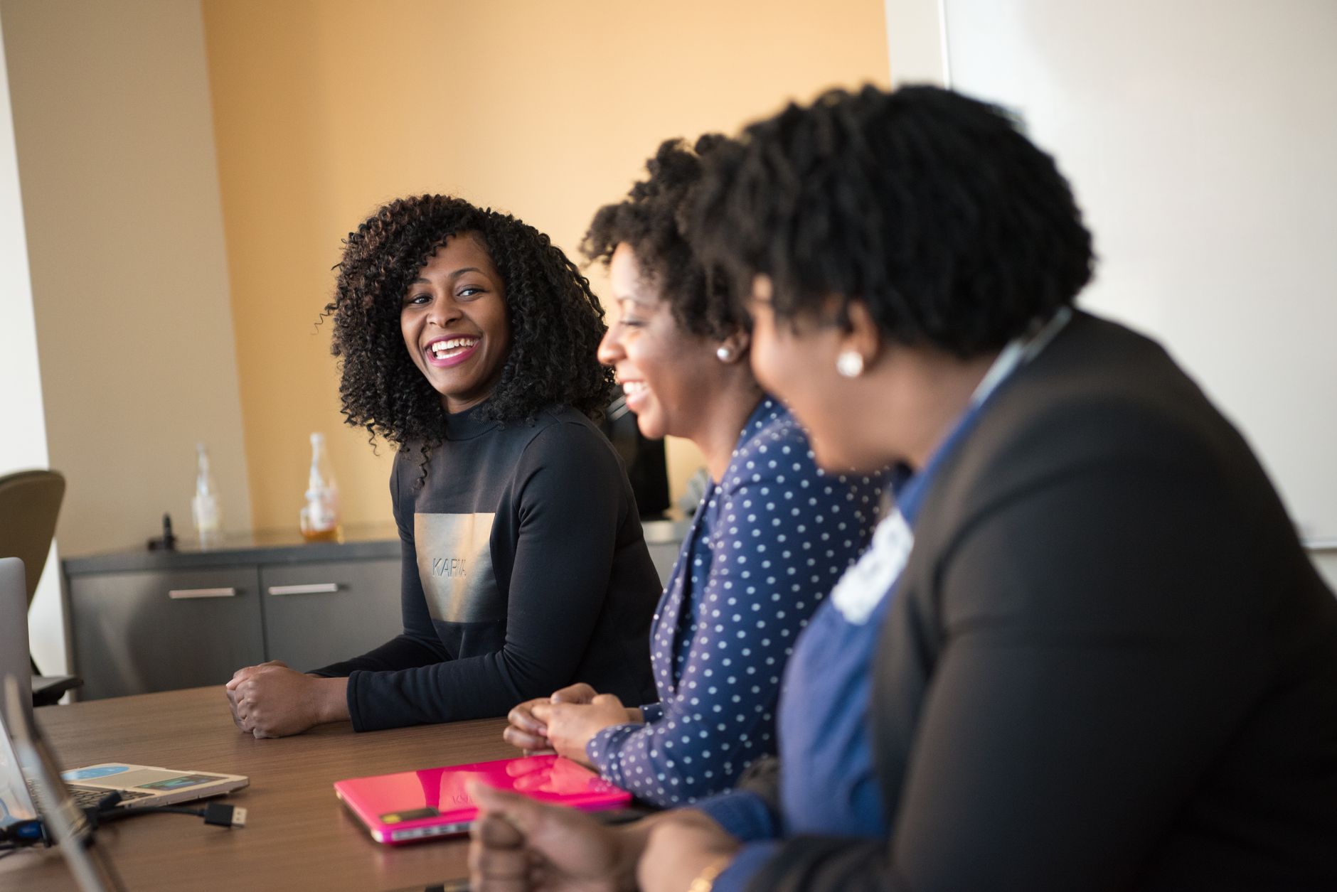 Three women laugh together around a meeting-room table
